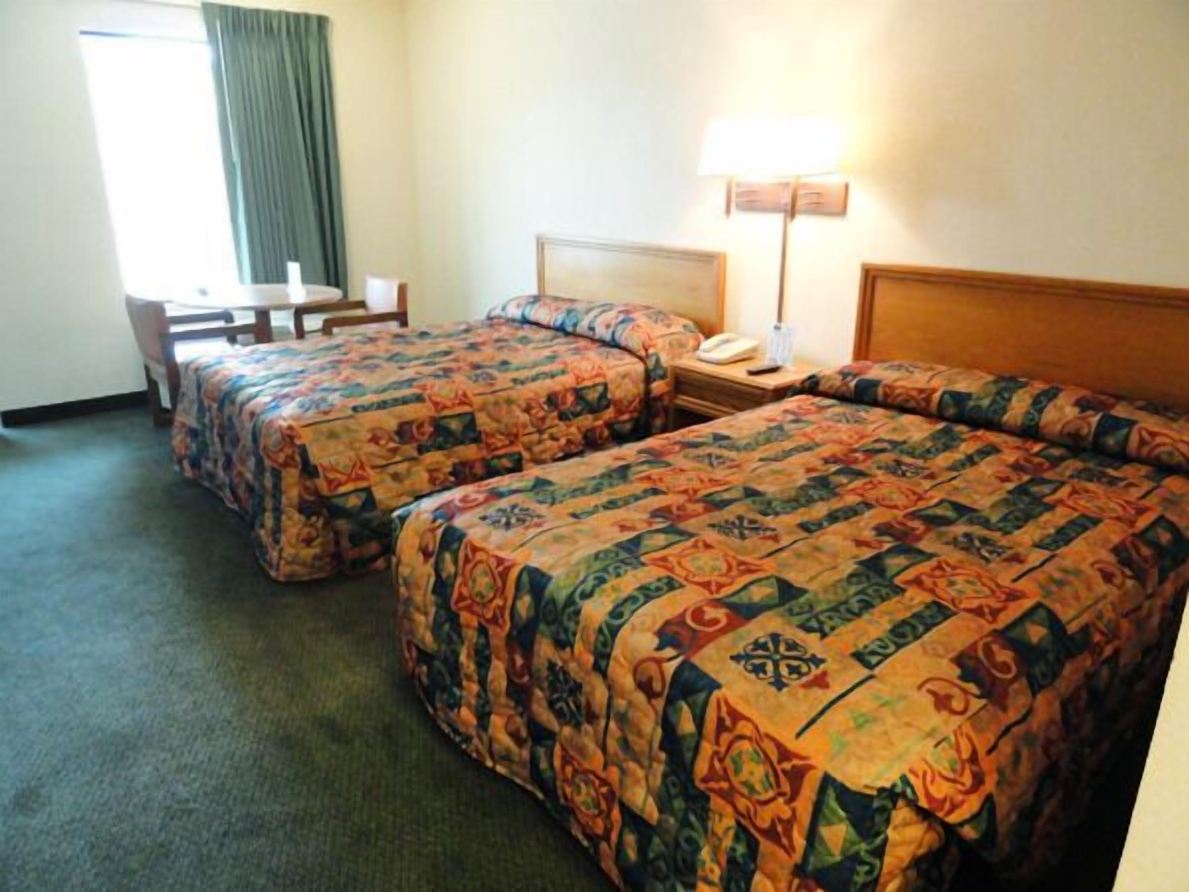 Ein Hotelzimmer mit zwei Betten, einem Schreibtisch und einer Lampe.