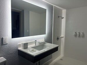 A modern bathroom with a large mirror, a white sink, and a shower area.