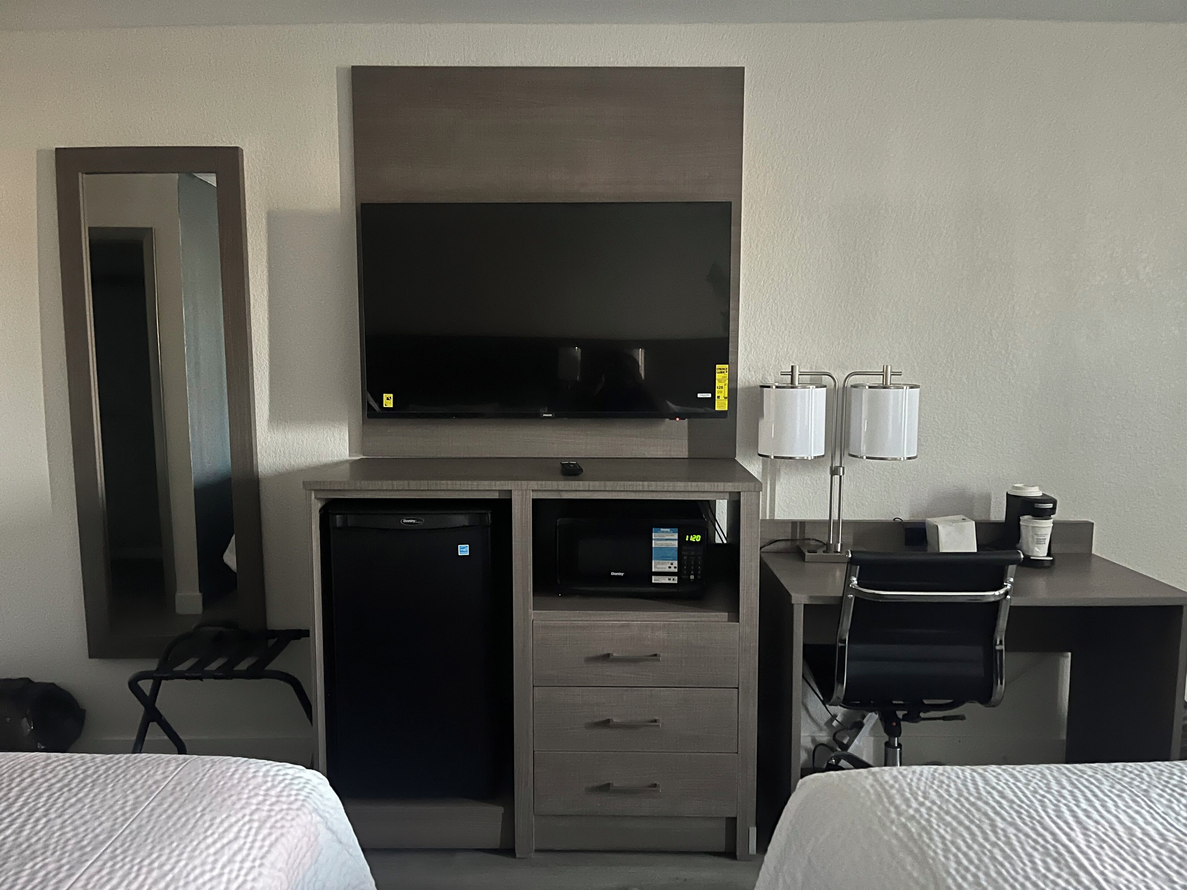 Habitación de hotel con cama, escritorio con computadora, televisor, microondas y cafetera.
