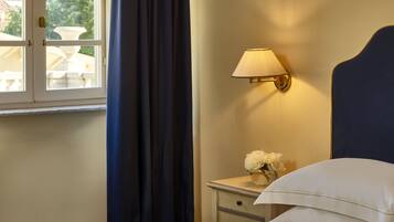A hotel room with a bed, a bedside table with a lamp, a vase with flowers, and a window with curtains.