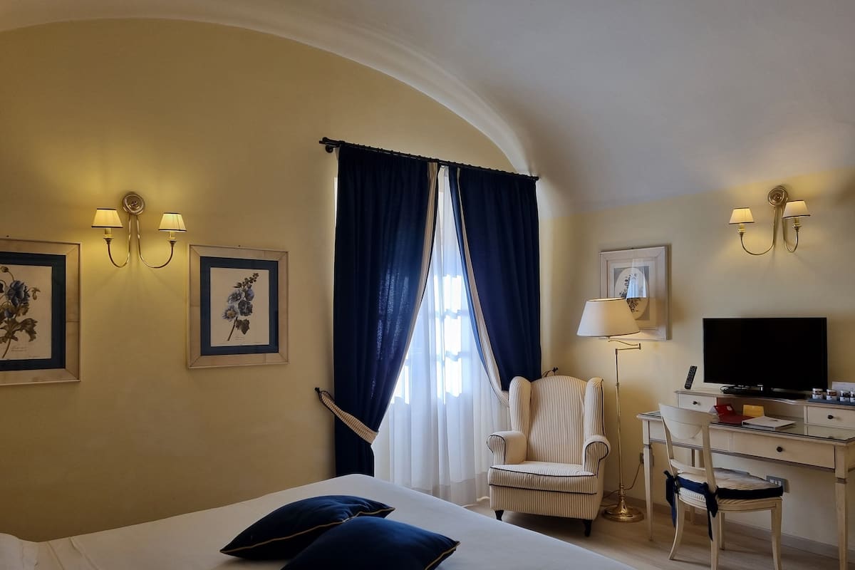A hotel room with a bed, two pillows, a chair, a desk with a television, and wall-mounted lamps.