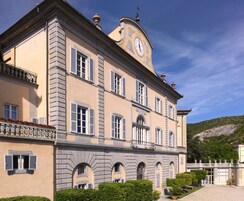 Un edificio storico con una torre dell'orologio, finestre simmetriche e un giardino curato.