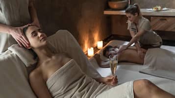Un'atmosfera rilassante in una spa, con una persona che riceve un massaggio alla testa, un'altra seduta con un drink e luci di candela.