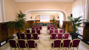 Una sala conferenze con file di sedie, un palco e piante in vaso.