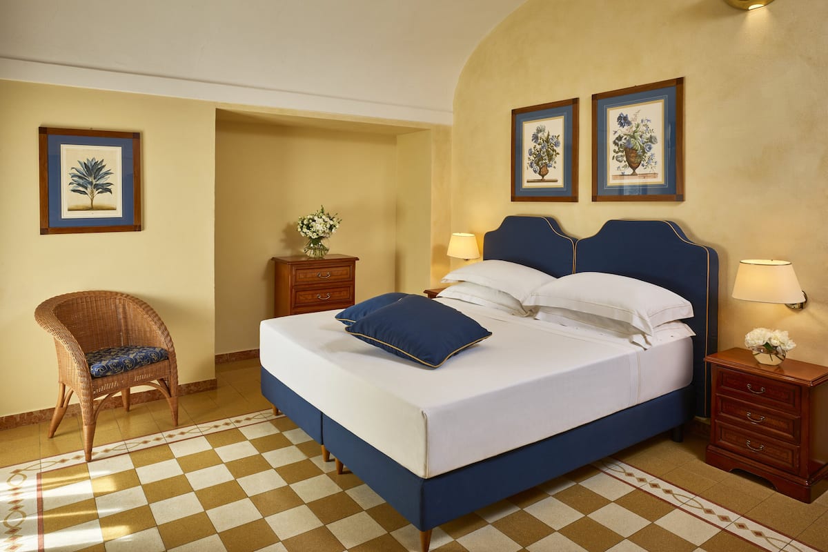 A bedroom with a large bed, a chair, a nightstand, and two wall-mounted lamps.