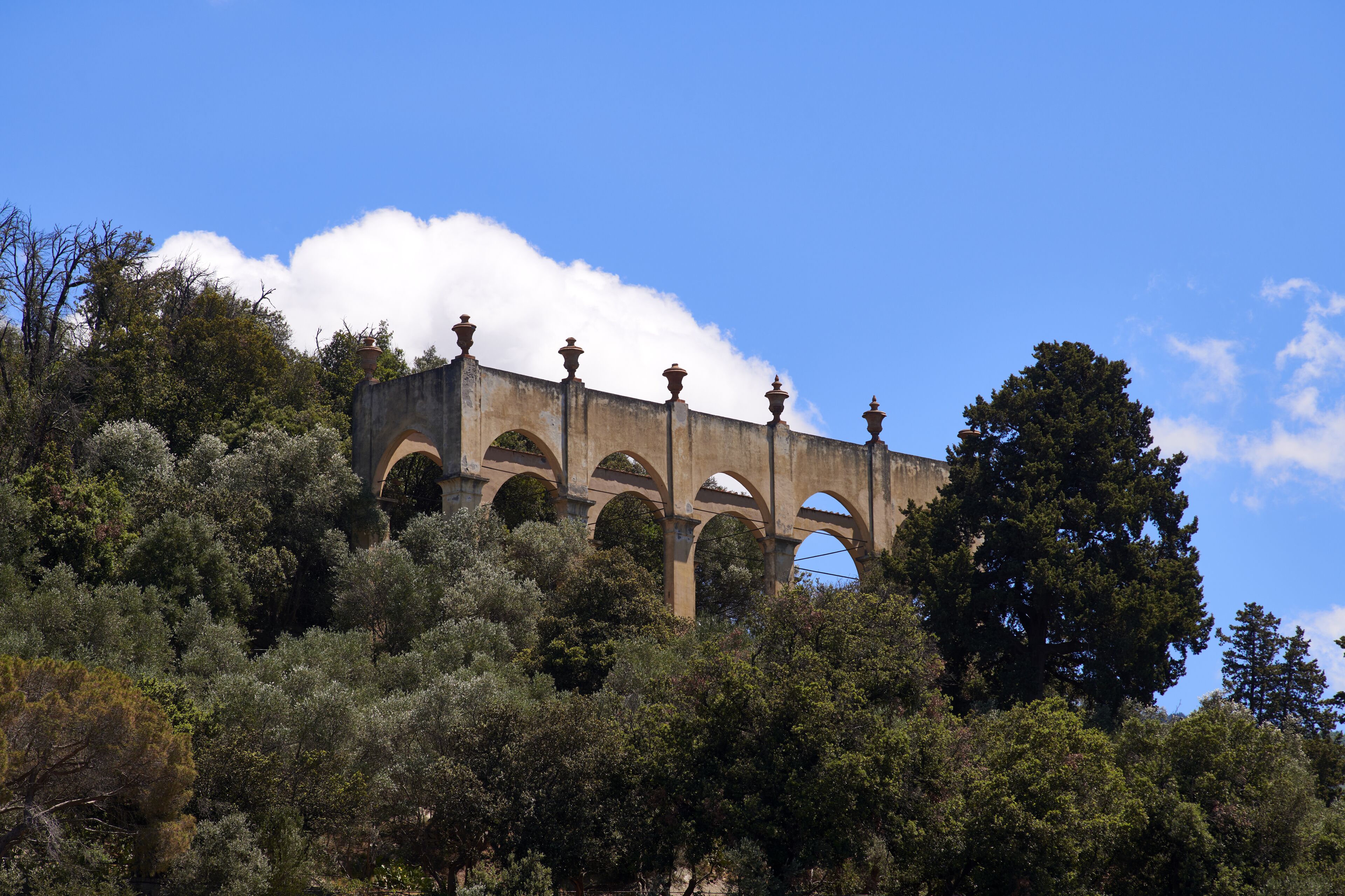 Edificio in pietra con archi e tetto piatto, circondato da alberi.