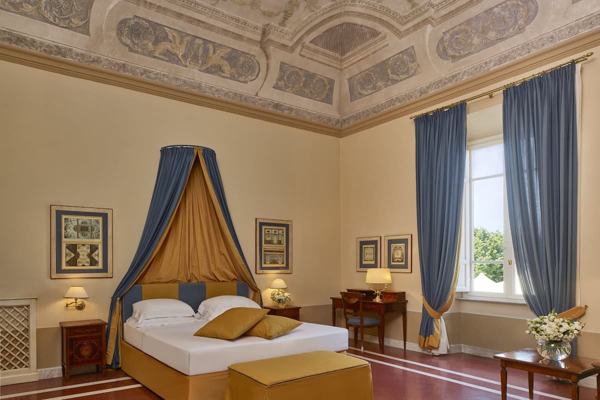 A room with a large bed, a desk, and a window with curtains.