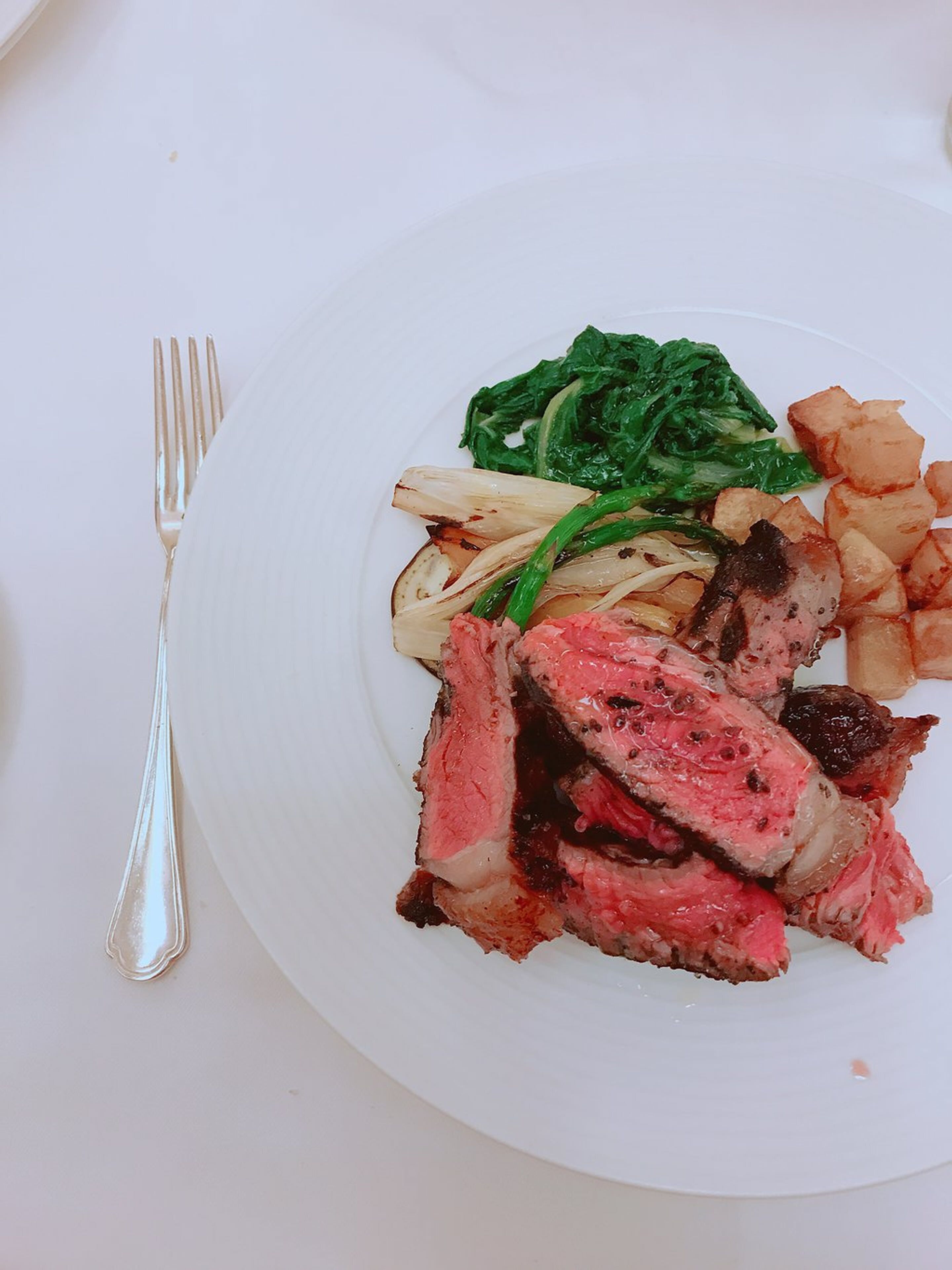 A plate with sliced steak, roasted potatoes, and greens.