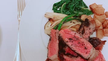 A plate with sliced steak, roasted potatoes, and greens.