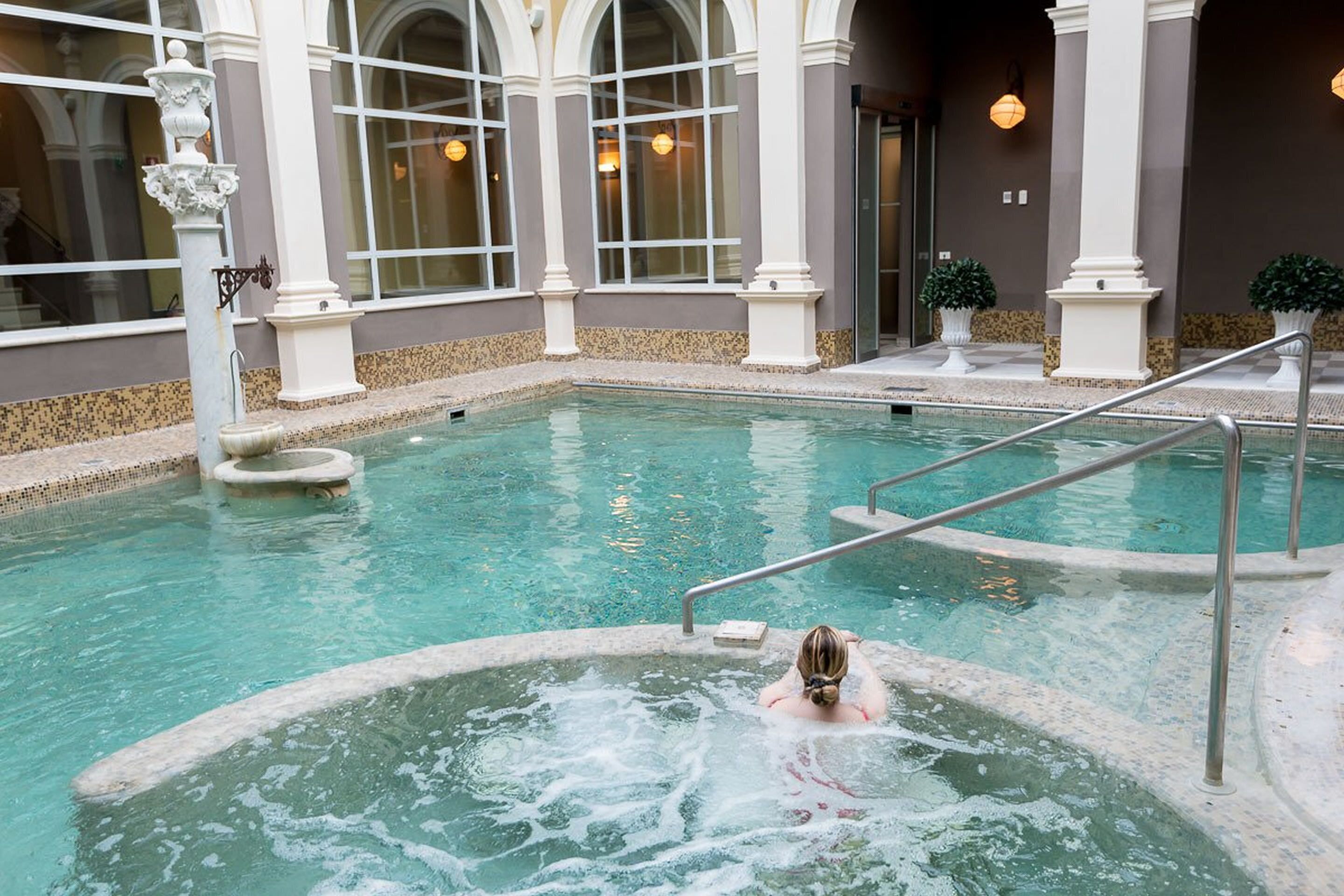 A pool area with a hot tub, steps leading into the pool, and a stone-tiled deck.