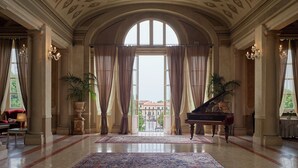 Een statige lobby met een groot, versierd plafond, een vleugelpiano en een groot raam met uitzicht op de stad.