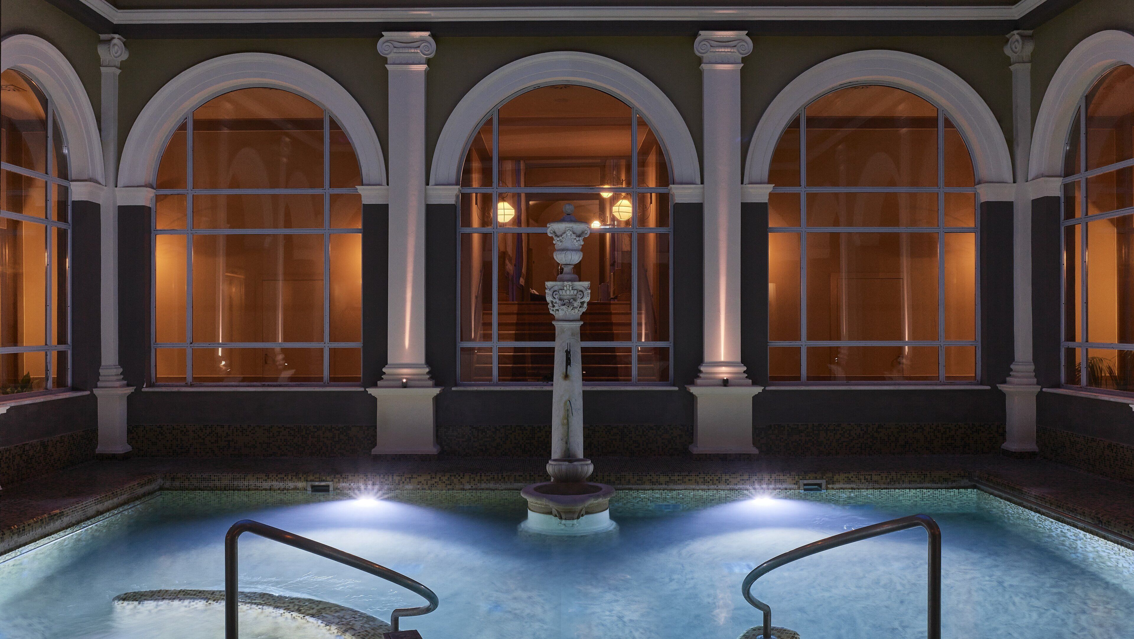 A pool area with a central fountain, surrounded by arched windows and columns.