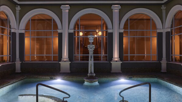 A pool area with a central fountain, surrounded by arched windows and columns.