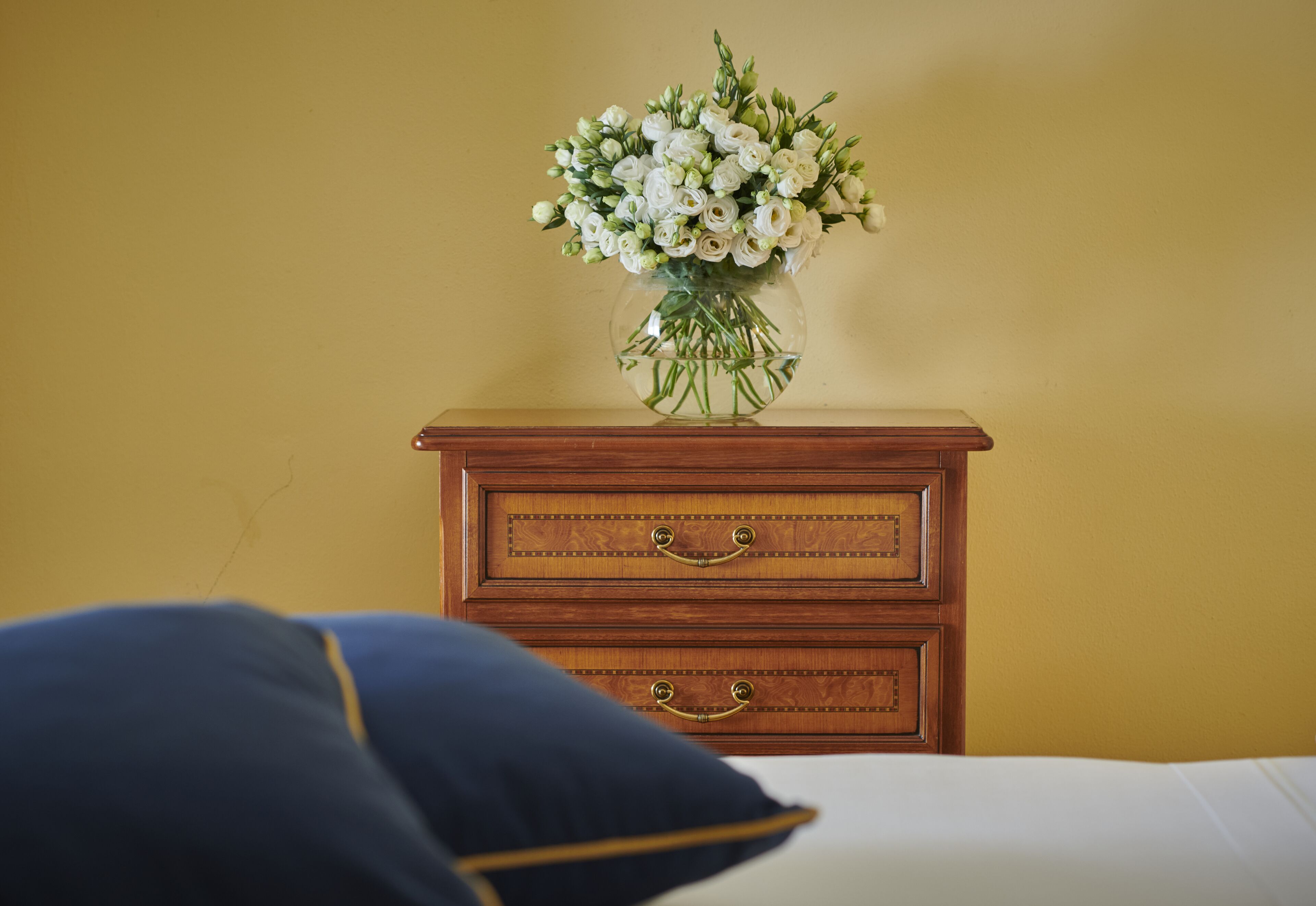 A wooden dresser with two drawers and a vase of white flowers on top.