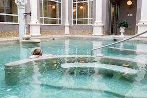 A pool with clear water, a person resting on the edge, and a building with large windows and columns in the background.