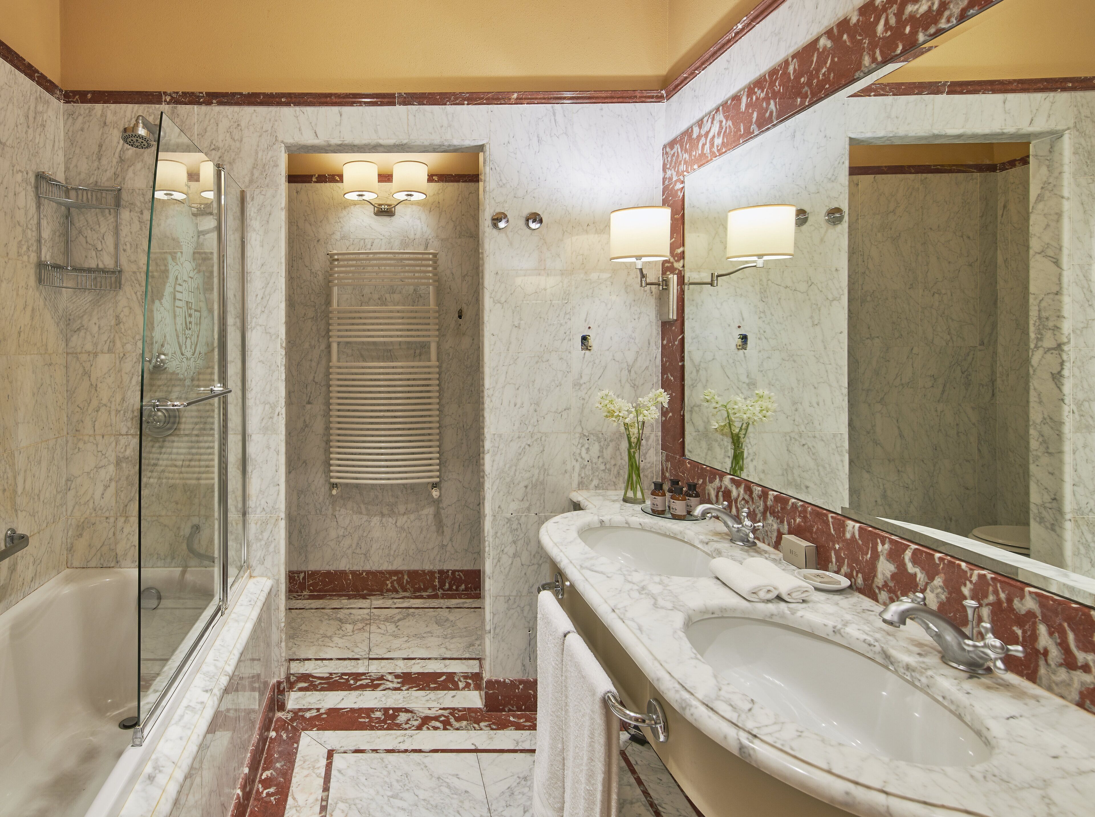 A bathroom with a glass-enclosed shower, a bathtub, and two sinks with a large mirror above.