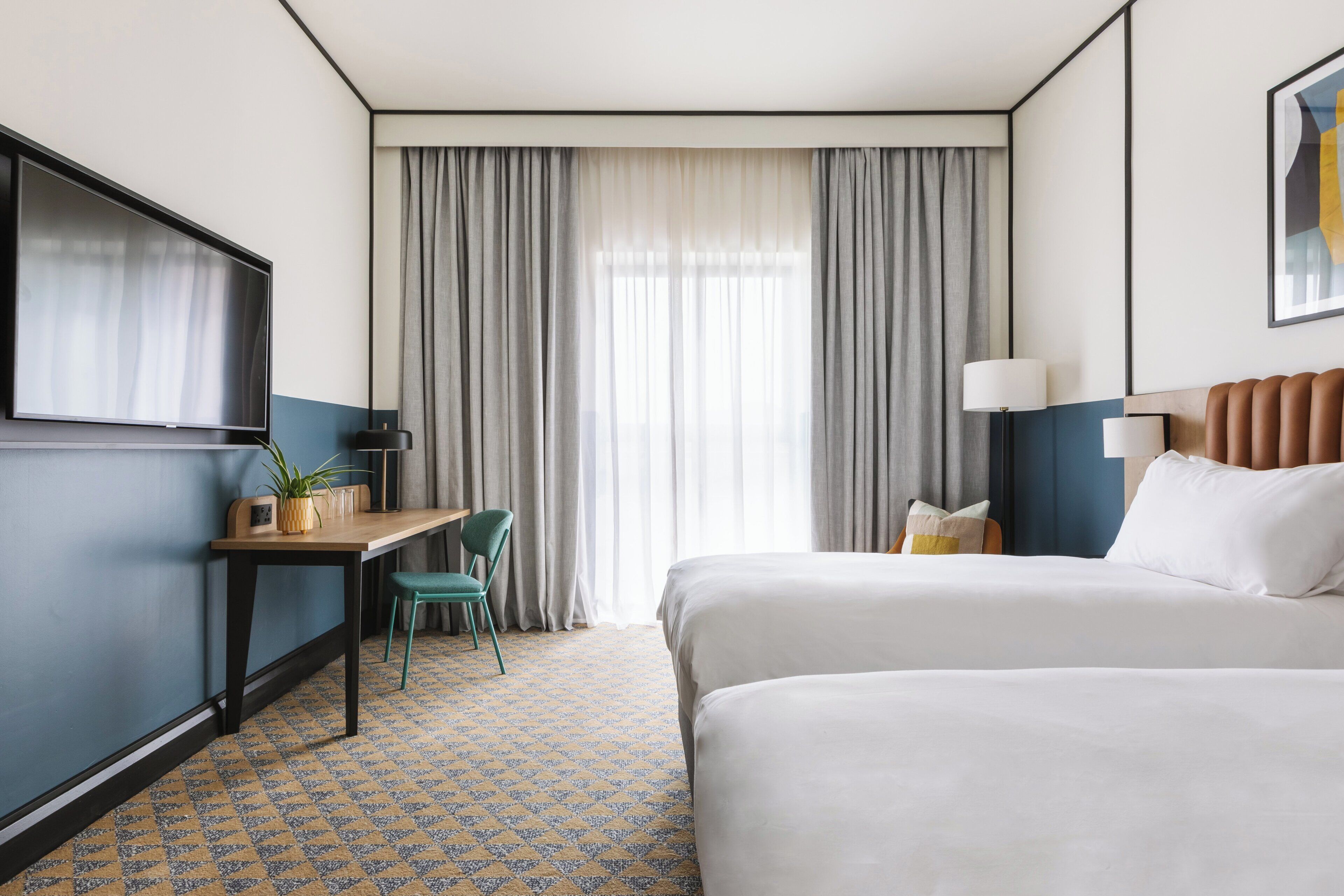 A hotel room with a bed, a desk, a chair, a TV, and a window with curtains.