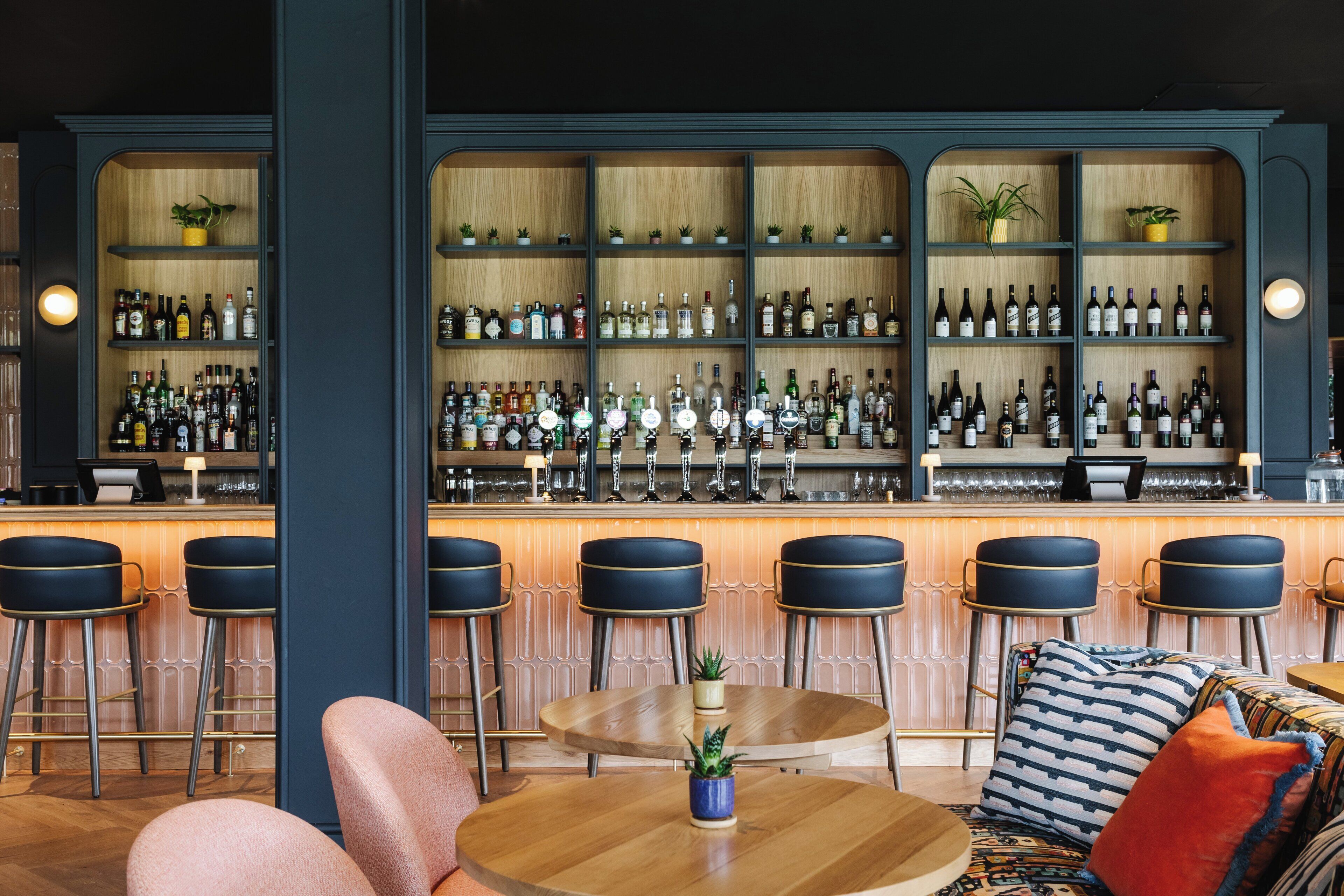 A bar area with multiple shelves of bottles, bar stools, and a round table with a plant.
