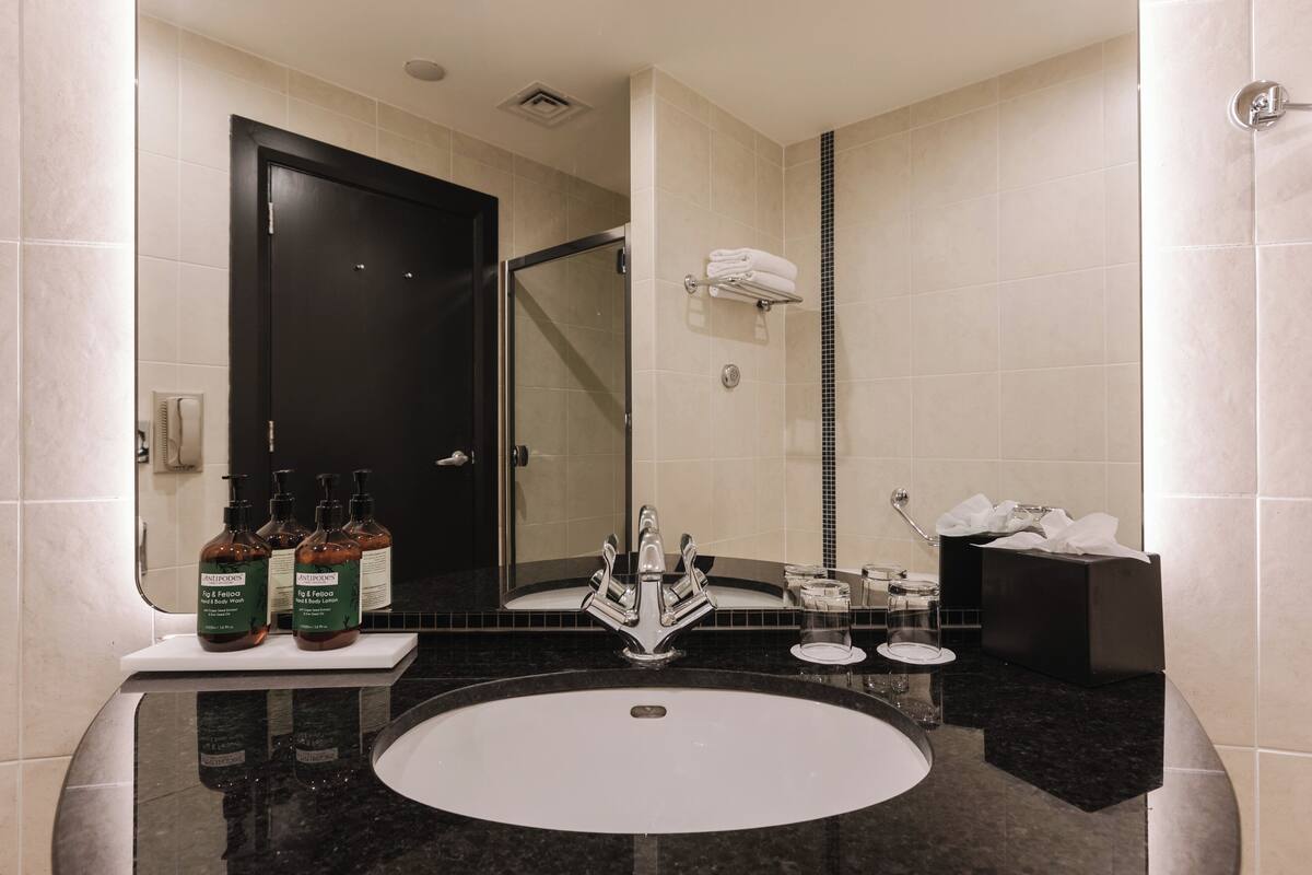 A bathroom with a black door, a glass shower enclosure, a white sink, and toiletries on the counter.