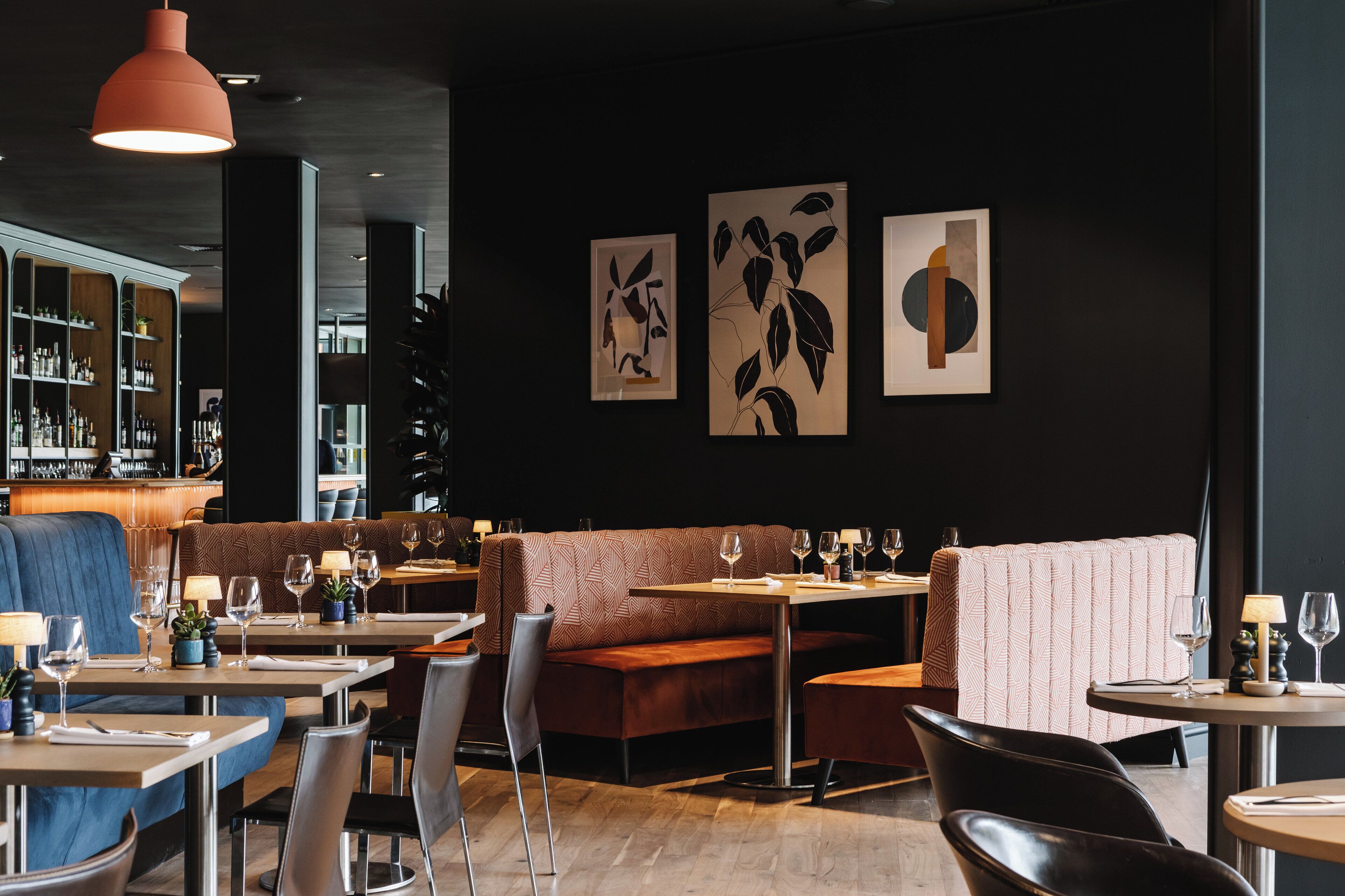 Ein modernes Restaurant mit Sitzecken und Tischen, einer Bar und Kunstwerken an den Wänden.
