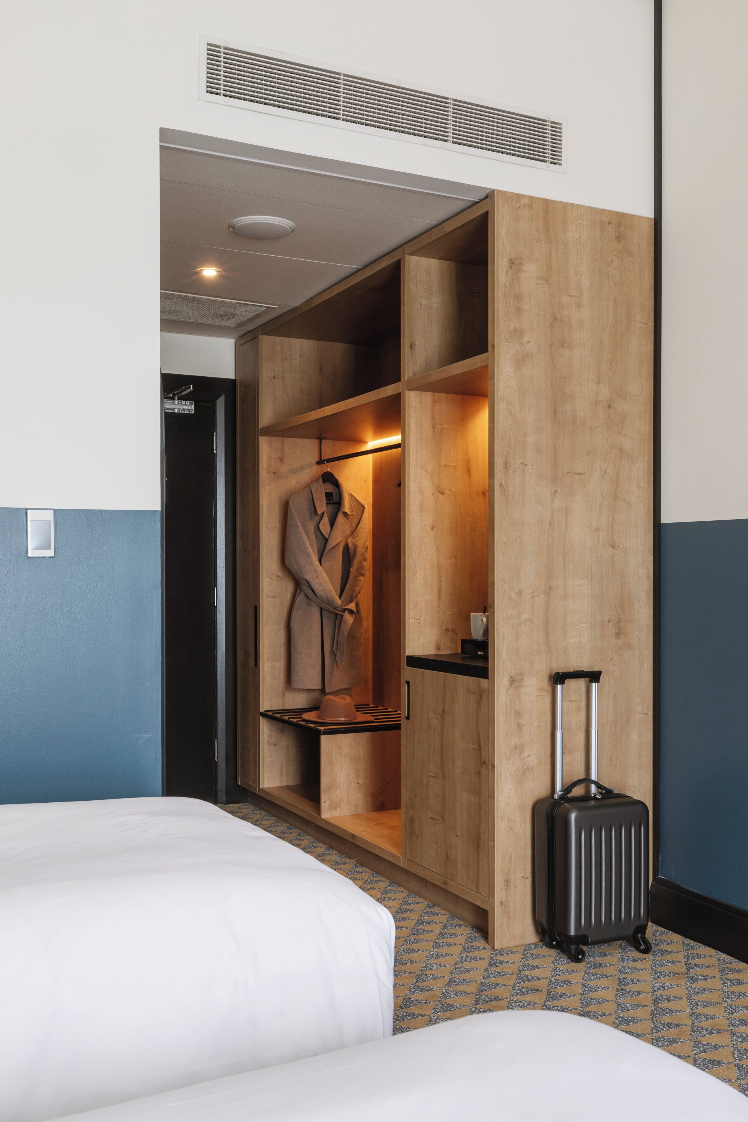 Ein Hotelzimmer mit einem Bett, einem Holzschrank, einem Koffer und einem Mantel, der im Schrank hängt.