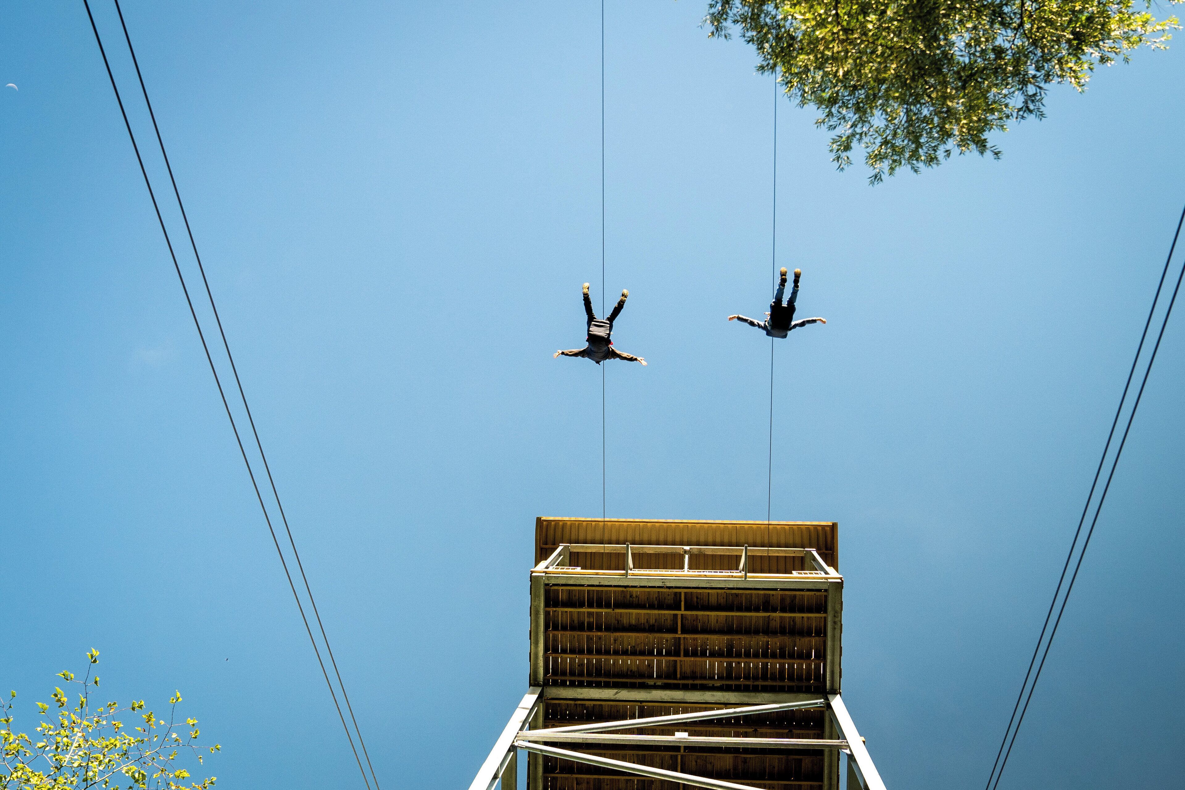 Two people suspended in mid-air, connected by ropes, against a clear blue sky.