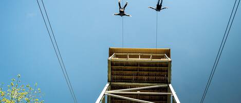 Two people suspended in mid-air, connected by ropes, against a clear blue sky.