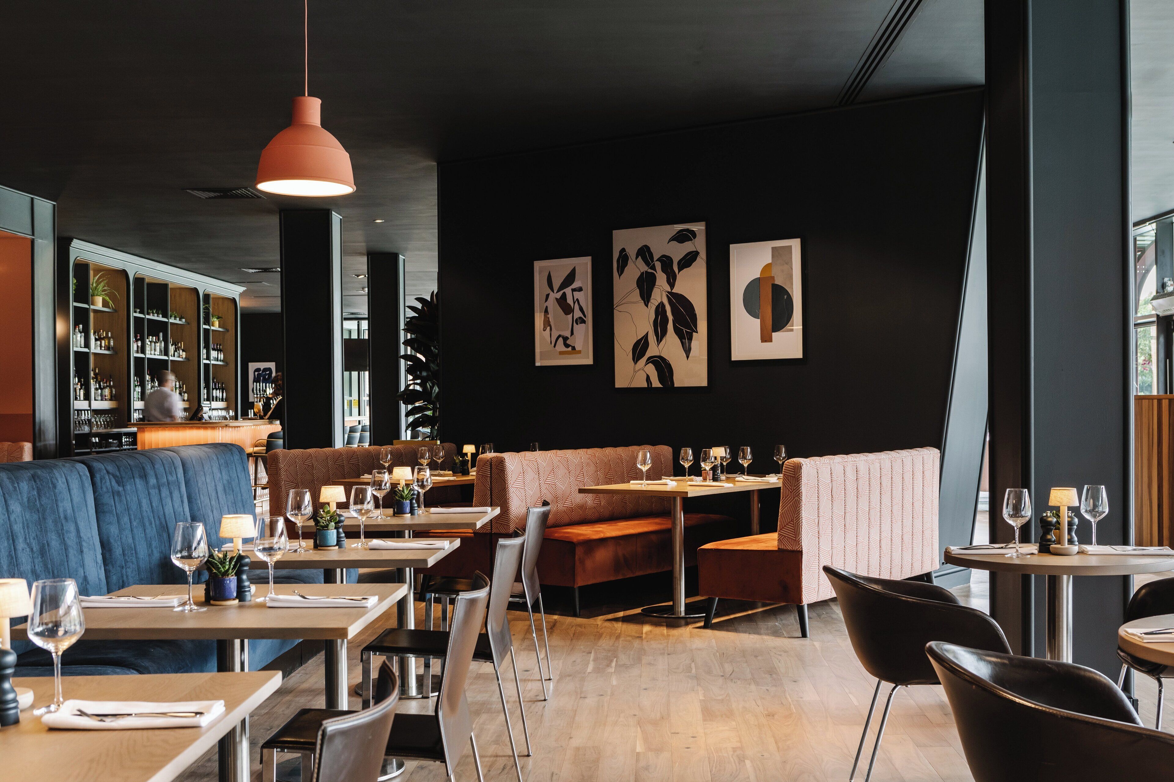 En moderne restaurantindretning med mørke vægge, blåt siddearrangement og kunst på væggene.