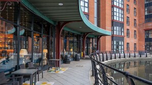 An outdoor seating area with tables and chairs, a curved glass enclosure, and a view of a building with large windows. - voco Belfast by IHG (Belfast)