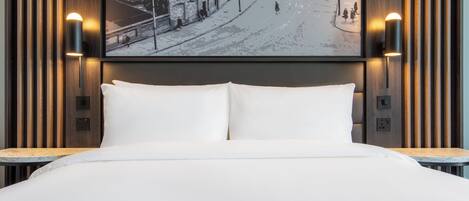 A hotel room with a large bed, two wall-mounted lamps, and a cityscape painting on the wall.