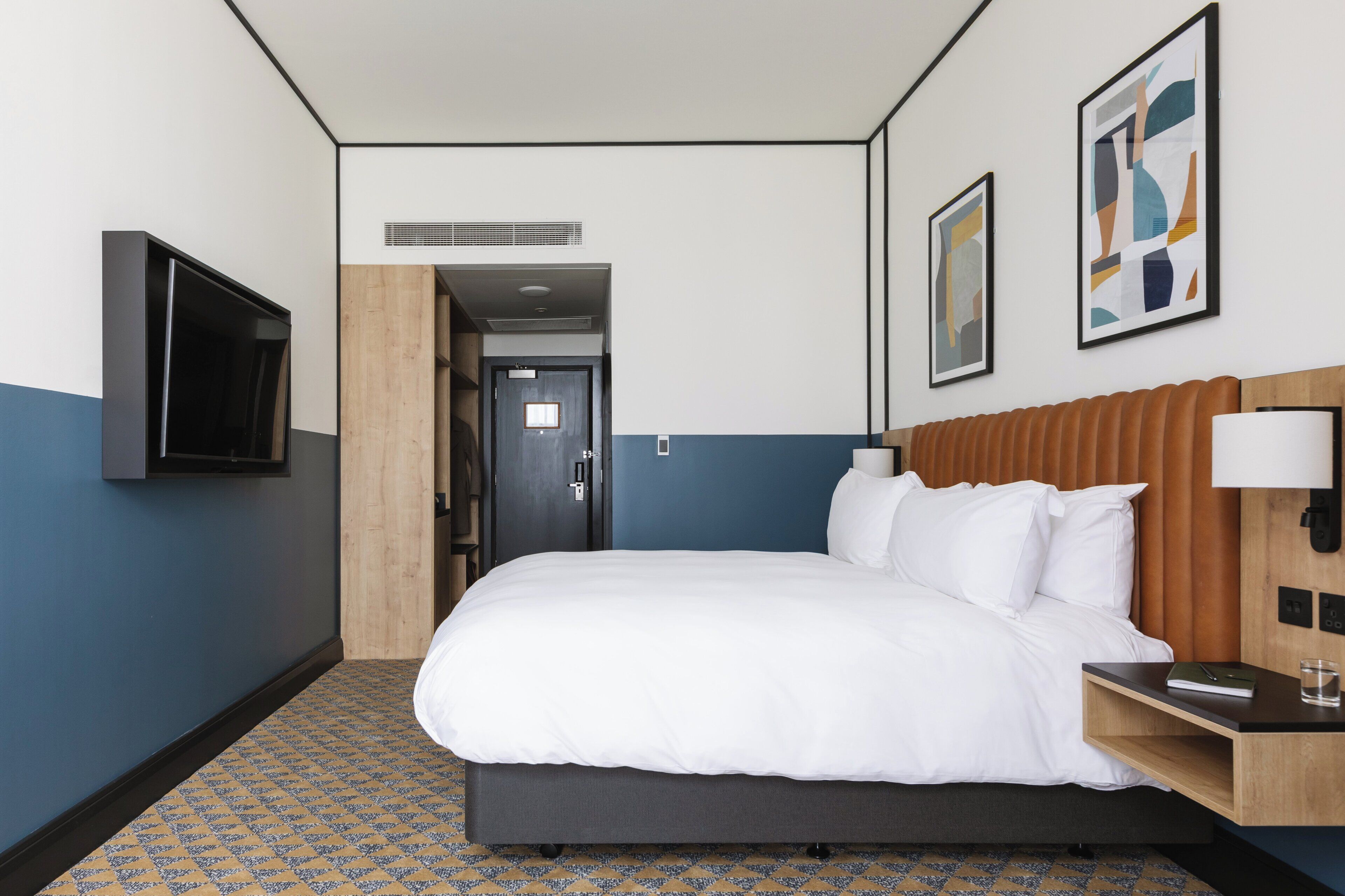 A hotel room with a large bed, a TV mounted on the wall, and artwork on the wall.