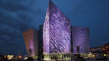 A modern building with a unique geometric facade, illuminated at night.