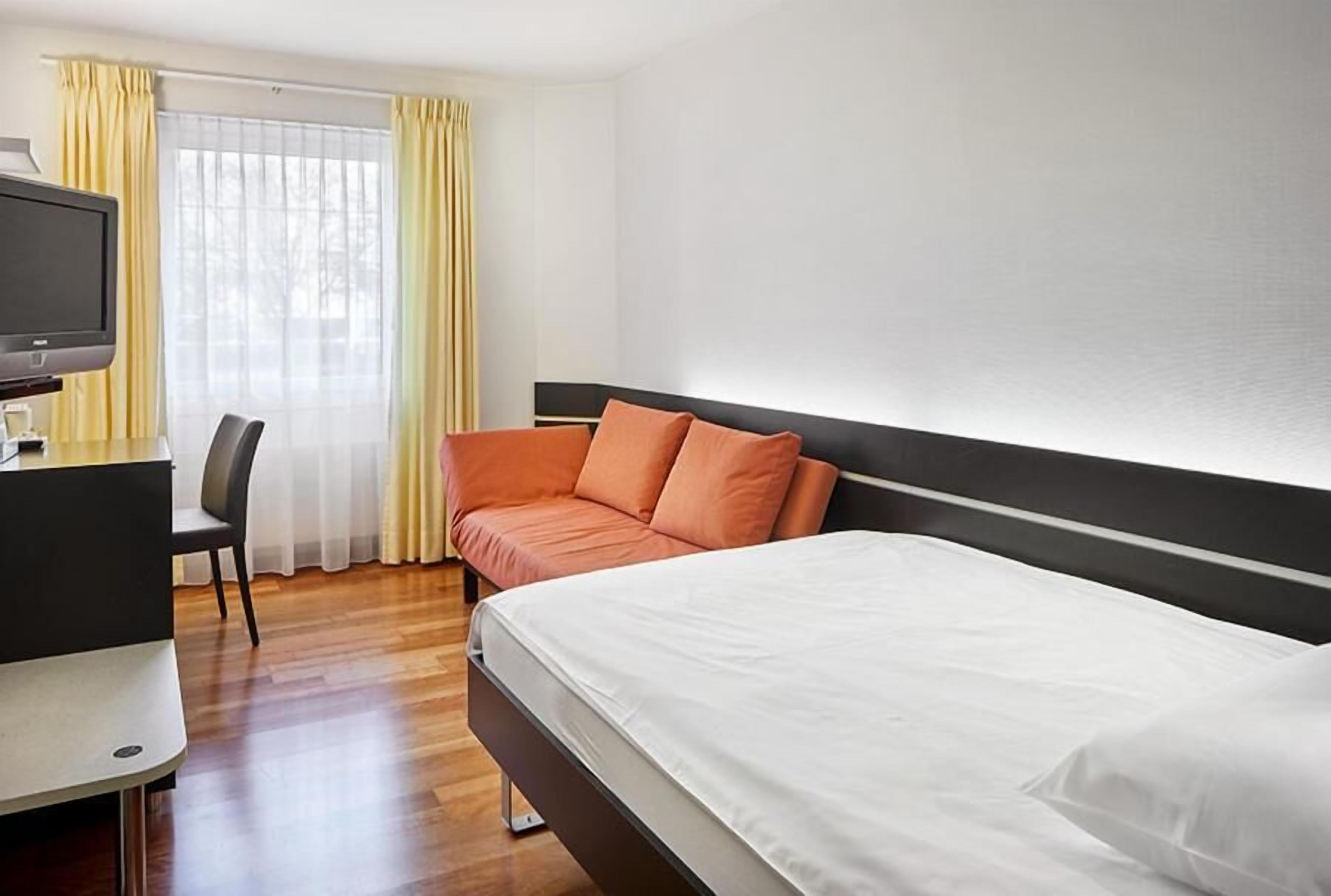 Una camera d'albergo con un letto, una scrivania con televisore e una sedia.
