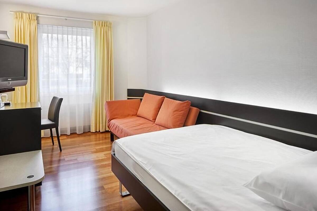 A hotel room with a bed, a desk with a television, and a chair.