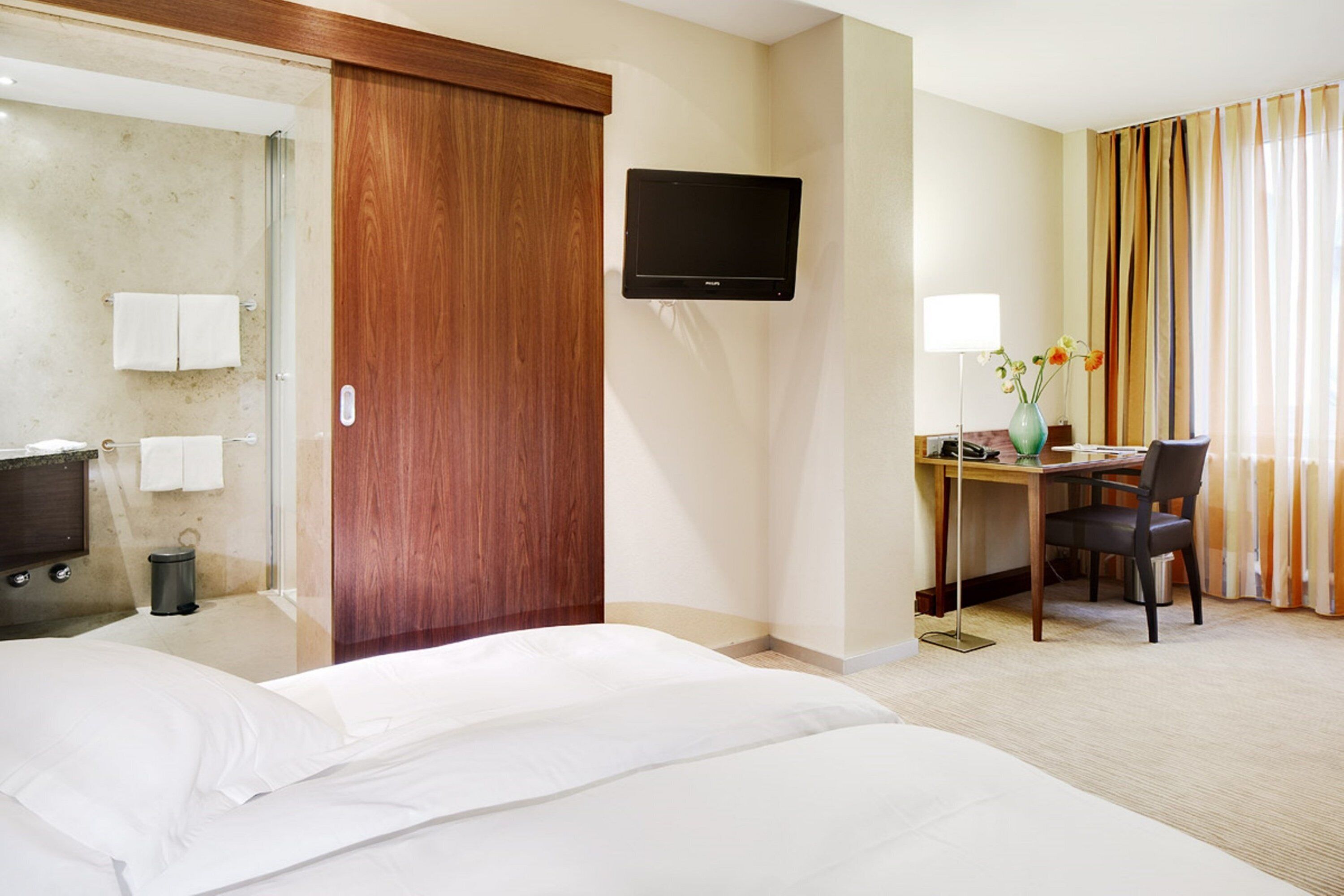 Ein Hotelzimmer mit Bett, Schreibtisch mit Stuhl, Fernseher und einem Badezimmer mit Dusche und Toilette.
