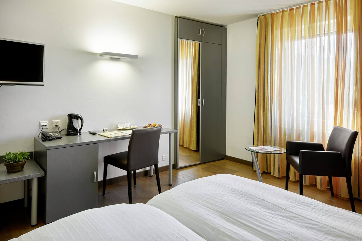 A hotel room with a bed, desk, chair, and a small table with a plant.