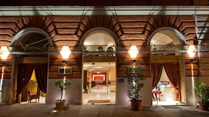 A hotel entrance with a brick facade, arched doorways, and potted plants. - c-hotels Fiume (Rome)