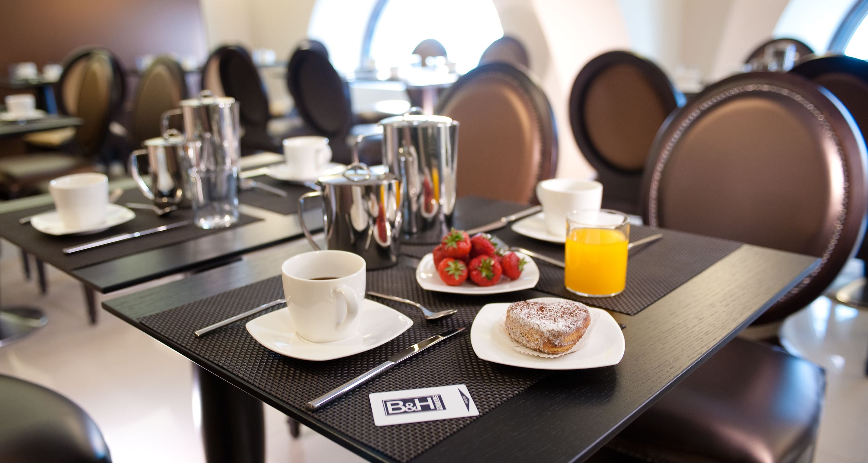 A breakfast setting with a coffee cup, a plate of strawberries, a pastry, and a glass of orange juice on a table.