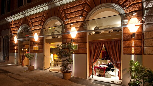 A hotel entrance with a brick facade, large arched windows, and potted plants. - c-hotels Fiume (Rome)