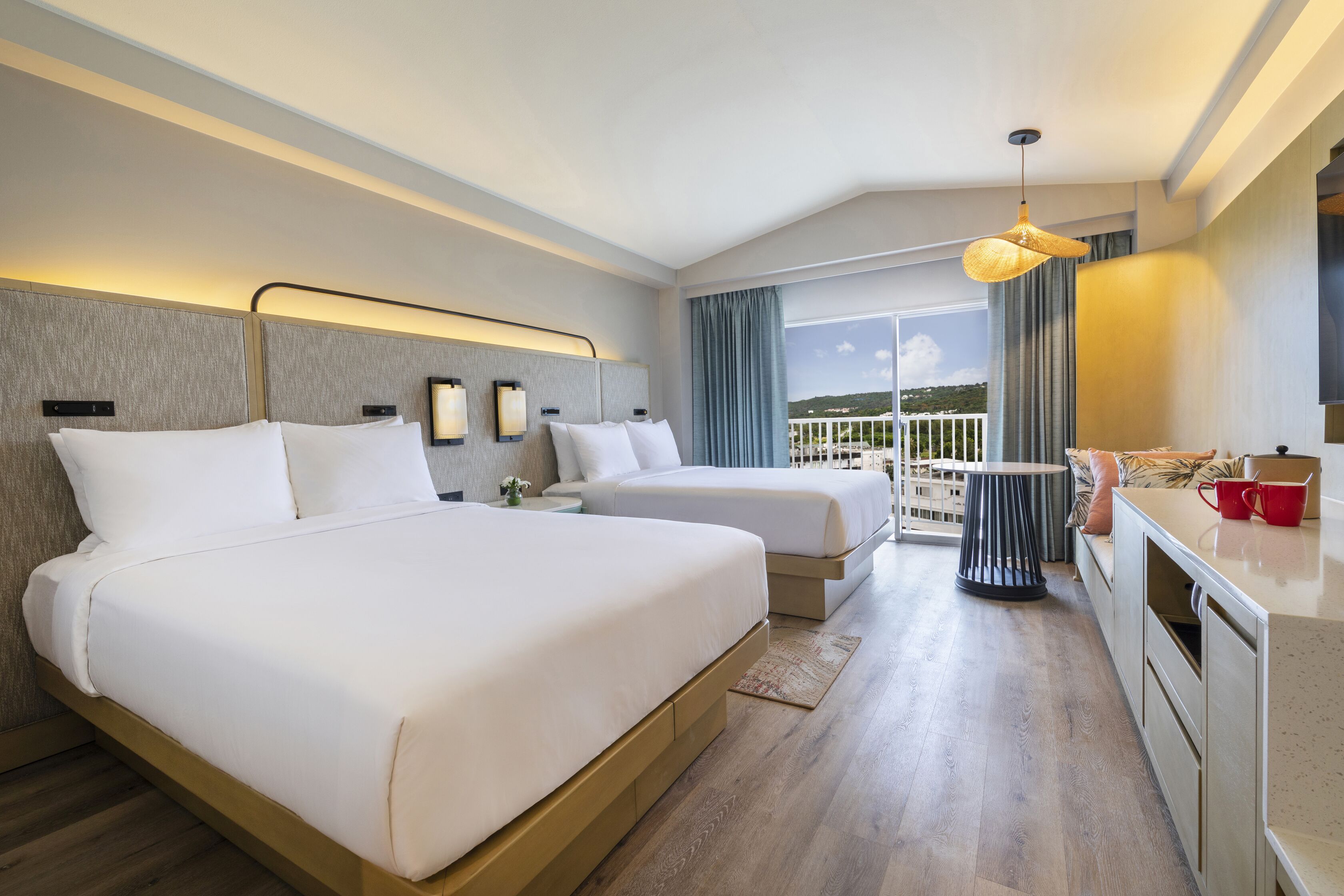 A hotel room with two beds, a kitchenette, and a balcony with a view.