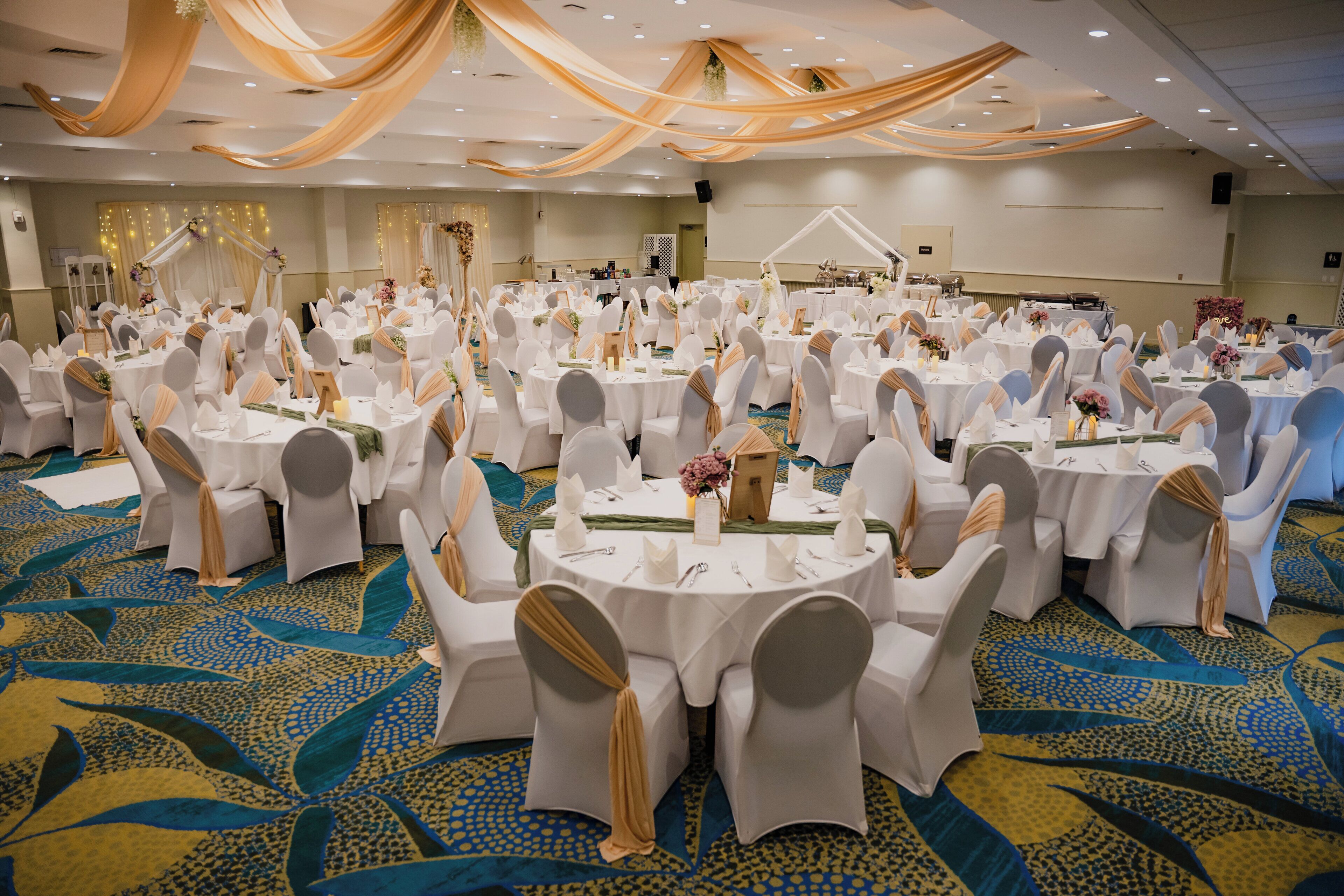 A banquet hall with round tables, white tablecloths, and chairs with gold sashes.
