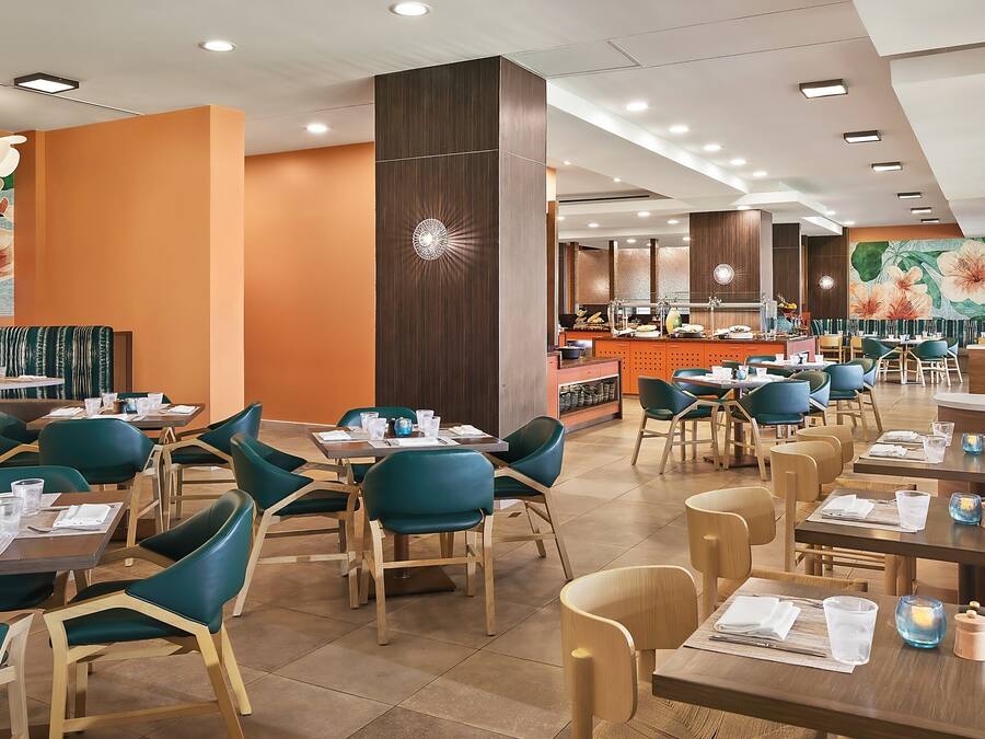 Un restaurante espacioso con varias mesas y sillas, una barra central y un gran mural floral en la pared.