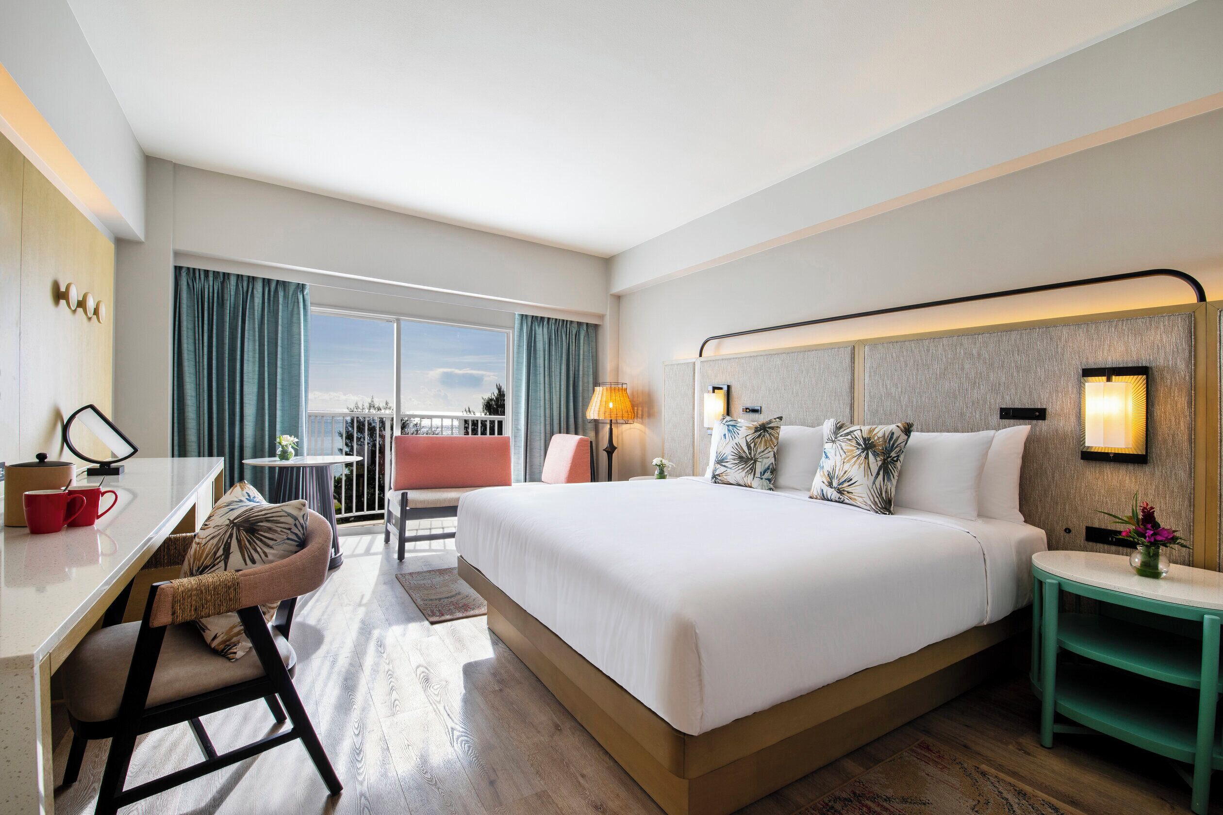 Een hotelkamer met een groot bed, een bureau met stoel, een kleine tafel met lamp en uitzicht op de omgeving.