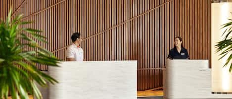 Un área de recepción con dos mostradores de mármol, una pared de listones de madera y una planta grande en maceta.