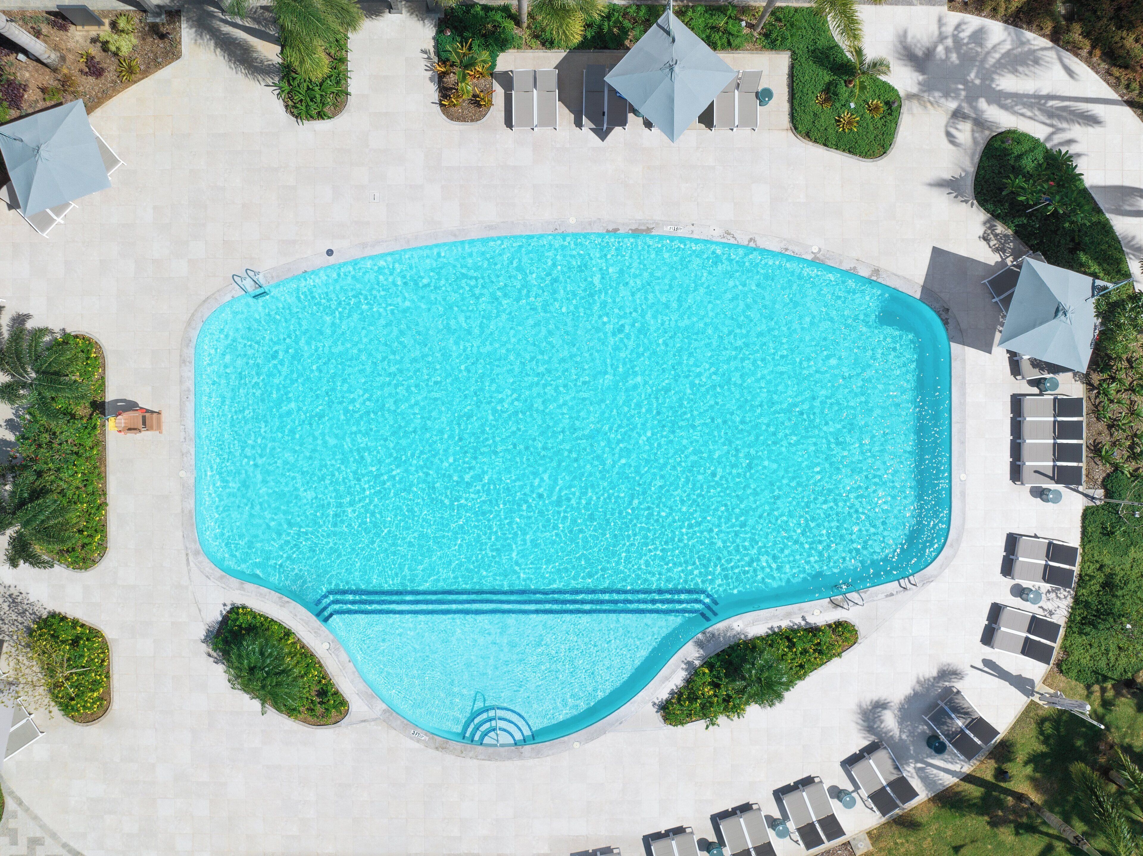 An aerial view of a rectangular swimming pool with a surrounding patio area, including lounge chairs and umbrellas.