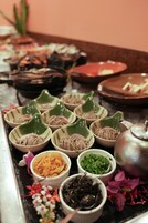 Una mesa con diversos platos e ingredientes, como cuencos de fideos, una tetera y pequeños recipientes con verduras y hierbas.
