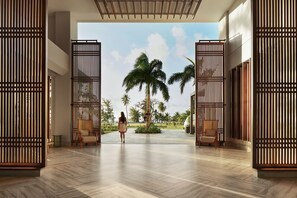 A spacious lobby with a modern design, featuring a large palm tree and a view of the outdoors.