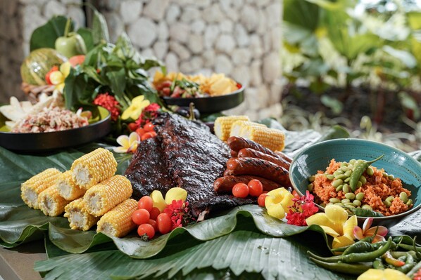 Diversos platos que incluyen carne a la parrilla, maíz y arroz, dispuestos sobre una hoja de plátano.