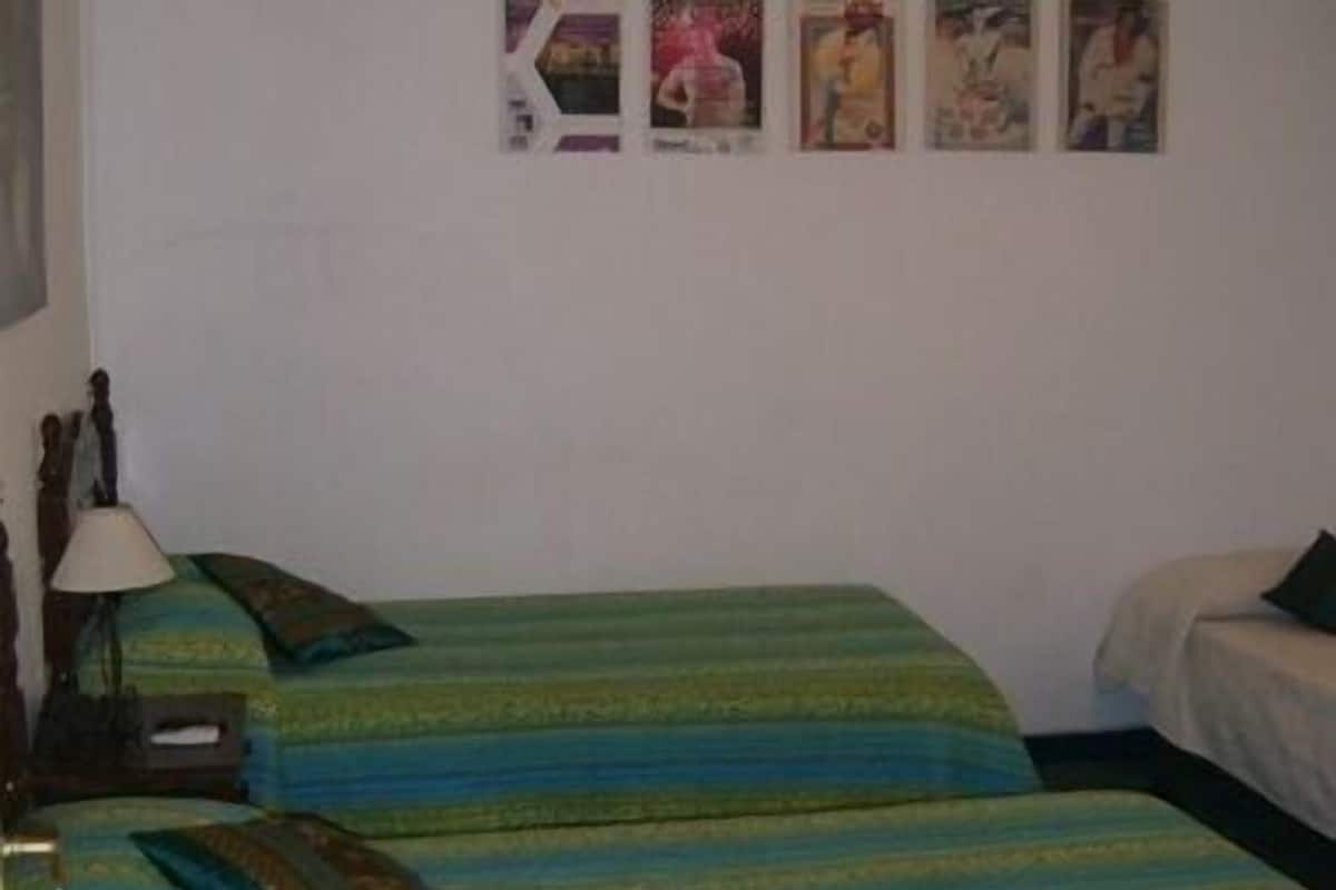 Habitación con dos camas, cada una con ropa de cama a rayas verdes y azules. Hay una lámpara en el lado izquierdo de la habitación.