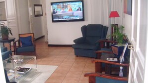 Una sala de estar con televisor, dos sillones, una mesa de centro y una lámpara roja.